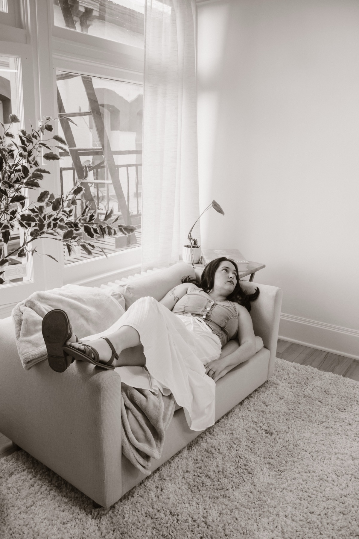 Black and white lounge portrait beside tall studio windows.